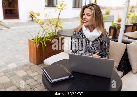 Middle-aged business woman working on a laptop in a street cafe and looking away Stock Photo