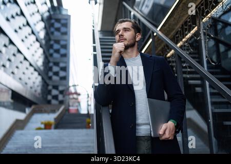 Pensive male head on the background of the city business center with a laptop in his hands, Concept business planning Stock Photo