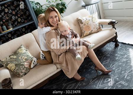 Happy mom fooling around with two boys sons sitting on sofa Stock Photo