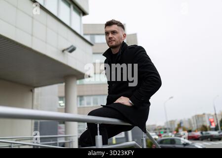 A very brutal man sits waiting for a meeting on the stairway parapet, his views fell into the distance Stock Photo