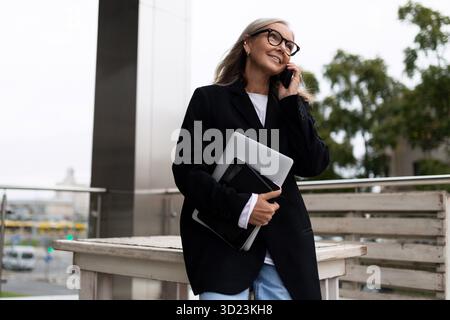Portrait of a successful business elderly Businessman with a laptop in his hands talking on a mobile phone Stock Photo
