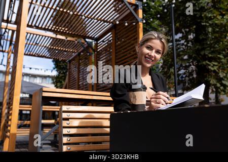 Successful businesswoman working outdoors drinking coffee and making notes in her diary Stock Photo