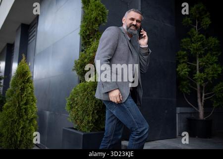 An elderly man businessman enters an office building talking on a mobile phone looking around with a smile Stock Photo