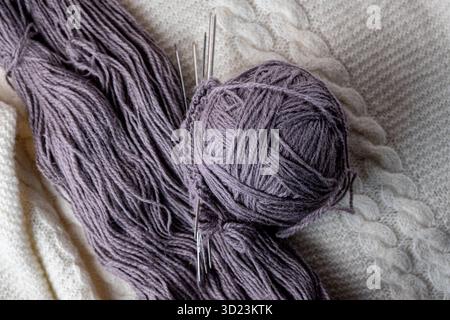 A ball of purple wool and knitting needles on a white background. Stock Photo