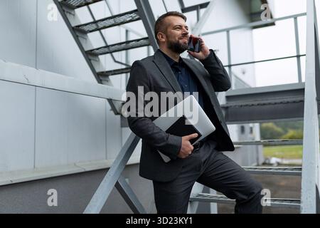 Caucasian business man in formal suit with laptop talking on the phone outside Stock Photo