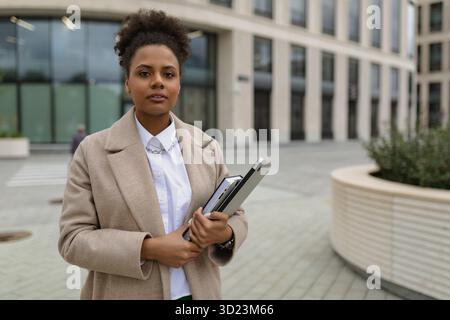 A woman of African American appearance, an official stands against the background of an administrative building with a laptop an Stock Photo