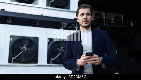 Air conditioner installation engineer on the background of industrial refrigeration equipment with a mobile phone in his hands Stock Photo