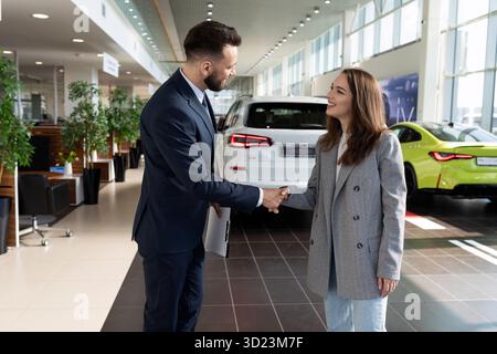 Young woman buyer and seller of car dealership making a deal and shaking hands Stock Photo