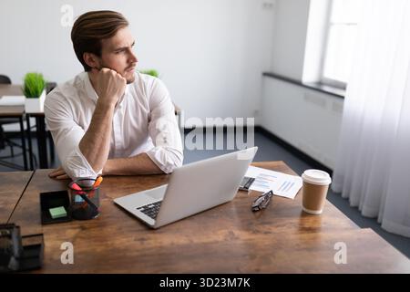 Pensive young businessman fills out an insurance form on laptops in the office Stock Photo