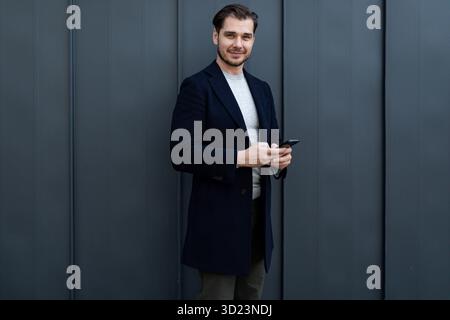 Successful middle-aged male businessman using a mobile phone against a gray wall Stock Photo