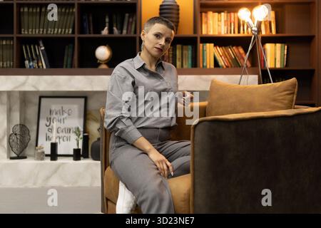 Stylish woman sitting in a cozy home environment in an armchair looking at the camera Stock Photo