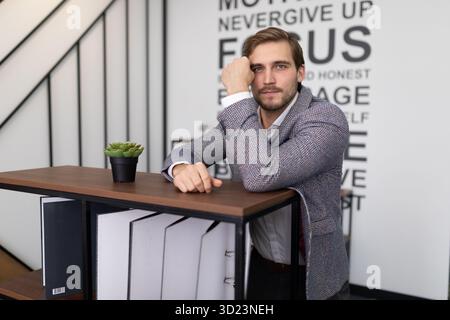 Thoughtful businessman stands leaning on a shelf with folders for documents in the office Stock Photo