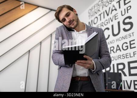 Young businessman making notes in a notebook while talking on a mobile phone in the office Stock Photo