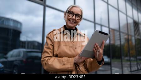 Elderly stylish woman with a tablet on the background of a business center, woman leader in business concept Stock Photo