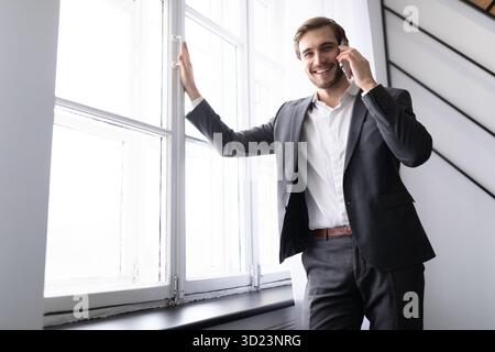 Young successful businessman speaks on the phone in a jacket at the window in the office Stock Photo