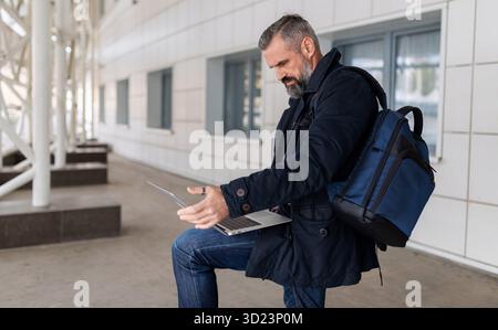 Mature male entrepreneur working on laptop online in airport lounge, freelance work concept Stock Photo