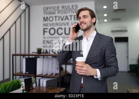 Business man in formal suit talking on the phone with a cup of coffee in his hands in the office Stock Photo