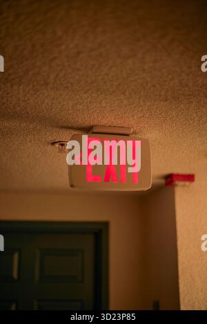 Red exit sign illuminated on a textured ceiling in a dimly lit hallway. California, USA Stock Photo