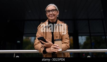 Portrait of a stylish fifty year old businesswoman with a phone and a cup of coffee in her hands Stock Photo