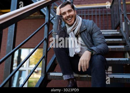 Charismatic smiling caucasian man he appearance sits on the steps and looks at the camera Stock Photo