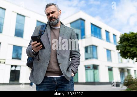 Adult male software engineer leaves the office and looks at the mobile phone Stock Photo