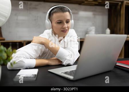 Business woman watching a webinar in headphones on a laptop while sitting at a table in the office Stock Photo