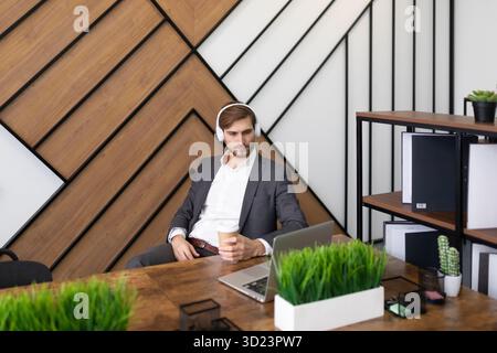 A man in an office wearing headphones listening to a training webinar Stock Photo