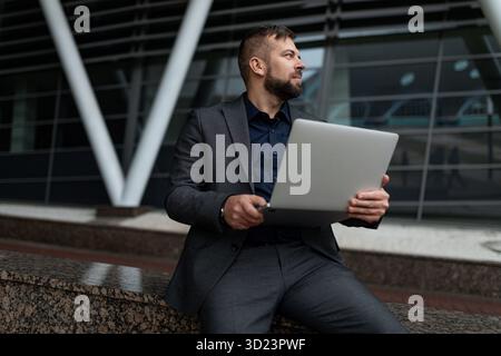 Man in business suit sitting working on laptop outside Stock Photo