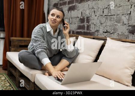Caucasian mature woman orders goods in online store by phone looking at laptop Stock Photo
