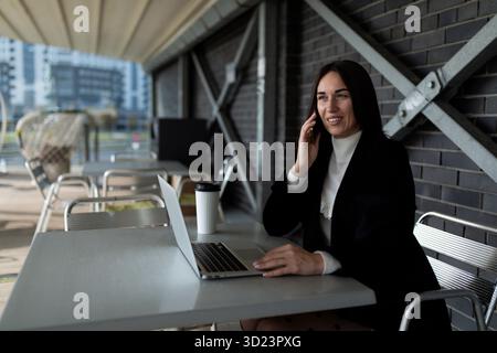 Businessman working on laptop online talking on mobile phone outside Stock Photo