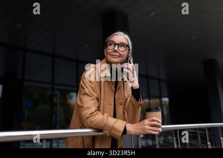 Adult business woman drinking coffee and talking on mobile phone outside Stock Photo