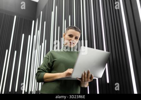 Successful woman programmer with a laptop in her hands with a short haircut against a gray wall Stock Photo