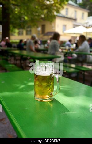 A glass of beer on a green table in an outdoor garden with people in the background. Munich, Germany Stock Photo
