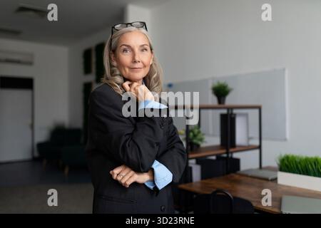 Successful caucasian Middle aged older businesswoman with glasses on her head in the middle of the office Stock Photo