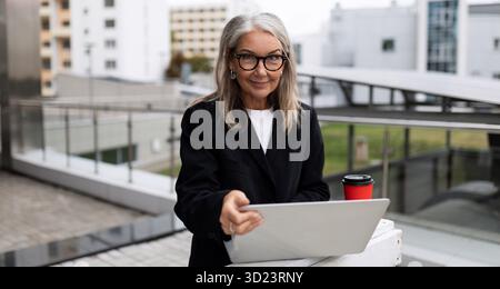 Stylish elderly manager working on laptop outside the office Stock Photo
