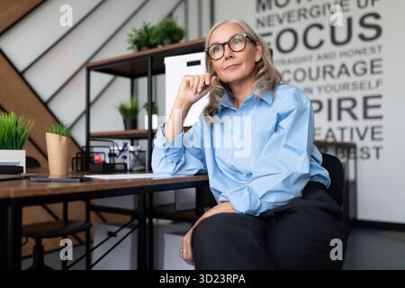 Middle aged older business woman in the office at the table looks thoughtfully into the distance Stock Photo