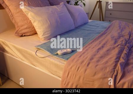 Modern electric heating pad on bed in room at night Stock Photo