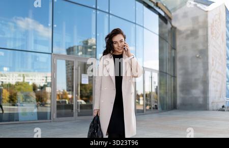 Strong female top manager comes out of the publication talking on a mobile phone Stock Photo