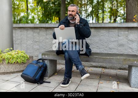 Mature man working on laptop outside talking on the phone Stock Photo