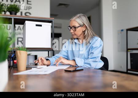 Mature business woman in a blue shirt works at a table in the office Stock Photo