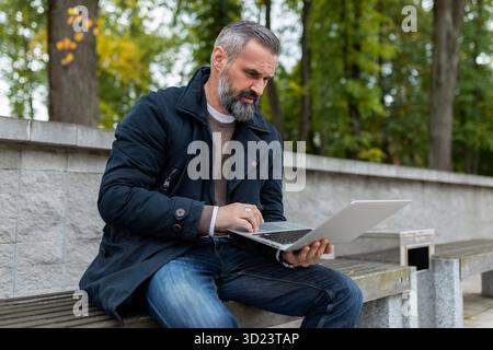 Gray-haired man working on a laptop in the park Stock Photo