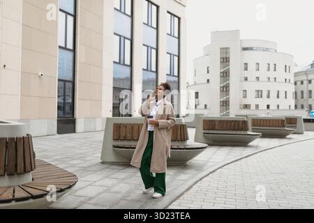 Business african american woman talking on mobile phone with cup of coffee outside office Stock Photo
