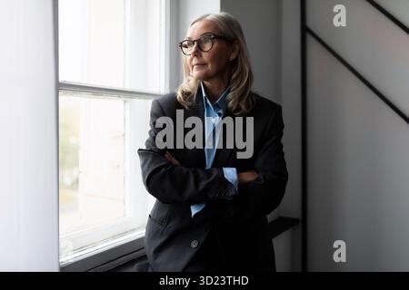 Experienced female stock market analyst in business clothes at the window in a modern office, evaluation of the effectiveness of Stock Photo