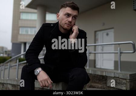 Stylish brutal man in a black coat on the background of the city Stock Photo