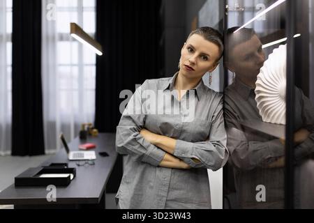 Tired serious woman head stands leaning against the wall in the office Stock Photo