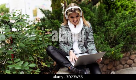 Business woman working on laptop with headphones outside Stock Photo