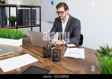 Manager works at a computer in glasses with papers on a table in a strong office Stock Photo