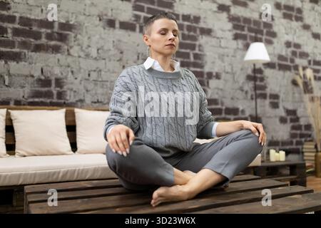 Adult caucasian woman meditating at home sitting in yoga pose Stock Photo