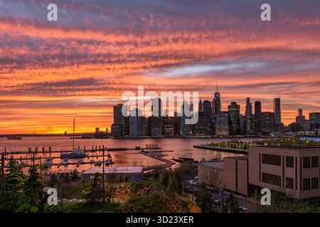 Sunset skyline over city with vibrant orange and pink hues reflected on the water. New York City, NY, USA Stock Photo