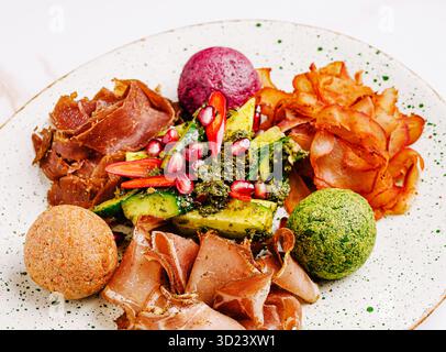 Assorted gourmet appetizer plate with cured meat, colorful cheese balls, avocado salad and vegetable chips Stock Photo